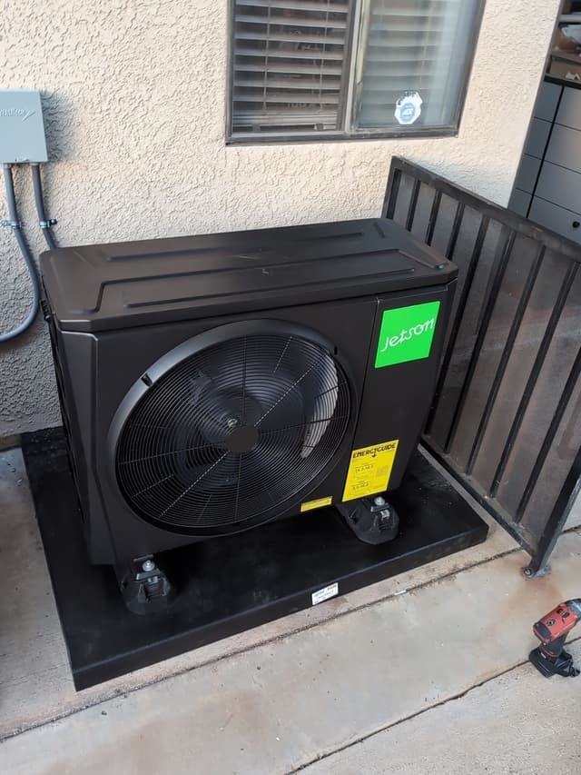 Jetson Air 2-ton heat pump condenser installed on a concrete patio against a tan stucco exterior wall in Walnut, CA, with electrical disconnect and conduit visible.