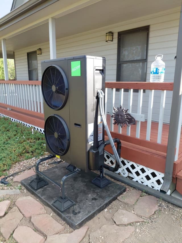 4-ton Jetson Air ducted heat pump on a metal riser stand beside a red-railed front porch, white siding and shrubbery in the background, Wellington, CO.