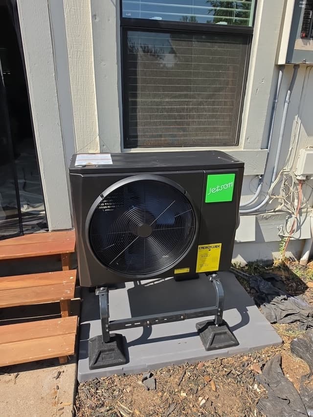 Black Jetson Air 2-ton central ducted heat pump outdoor unit installed against the side of a house in Westminster, with refrigerant lines running up the exterior wall.