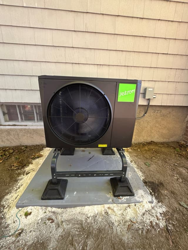 2-ton Jetson Air central ducted heat pump installed along the foundation of a grey-shingled home in Worcester, MA, with a disconnect box mounted on the siding.